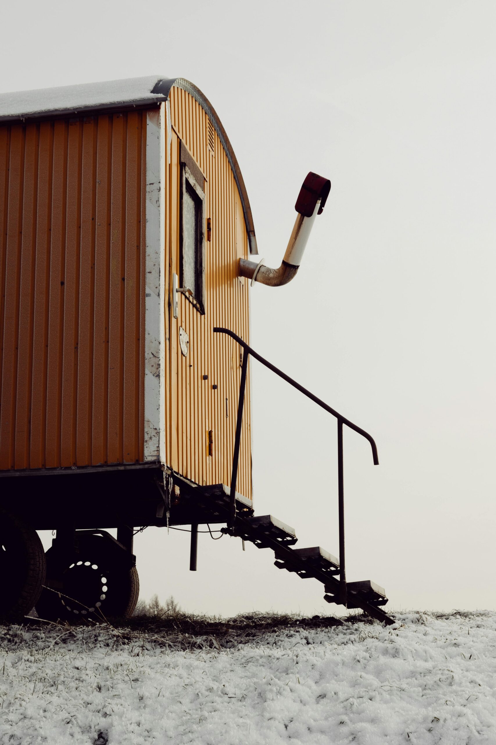 A vintage yellow caravan with a stovepipe sits on a snowy hill, capturing rustic charm.